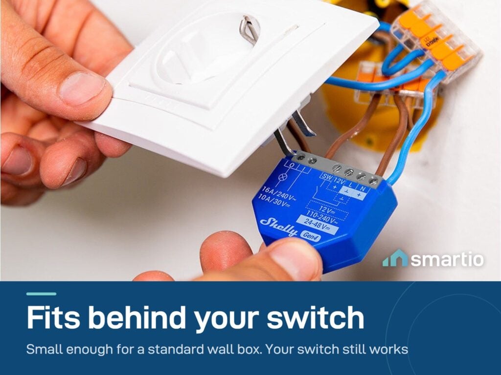 Hands fitting a Shelly 1 Gen4 module into the wall box behind a socket plate