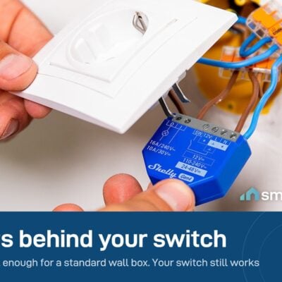 Hands fitting a Shelly 1 Gen4 module into the wall box behind a socket plate